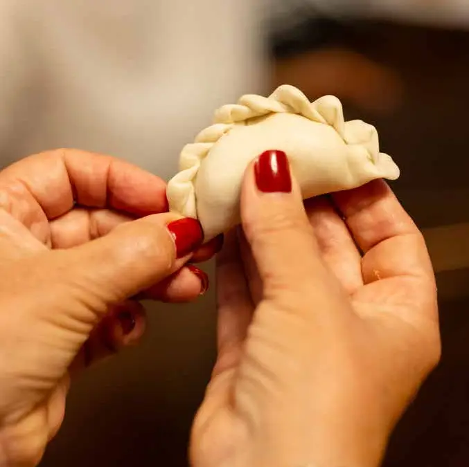 Hands pinching a varenyky dumpling closed